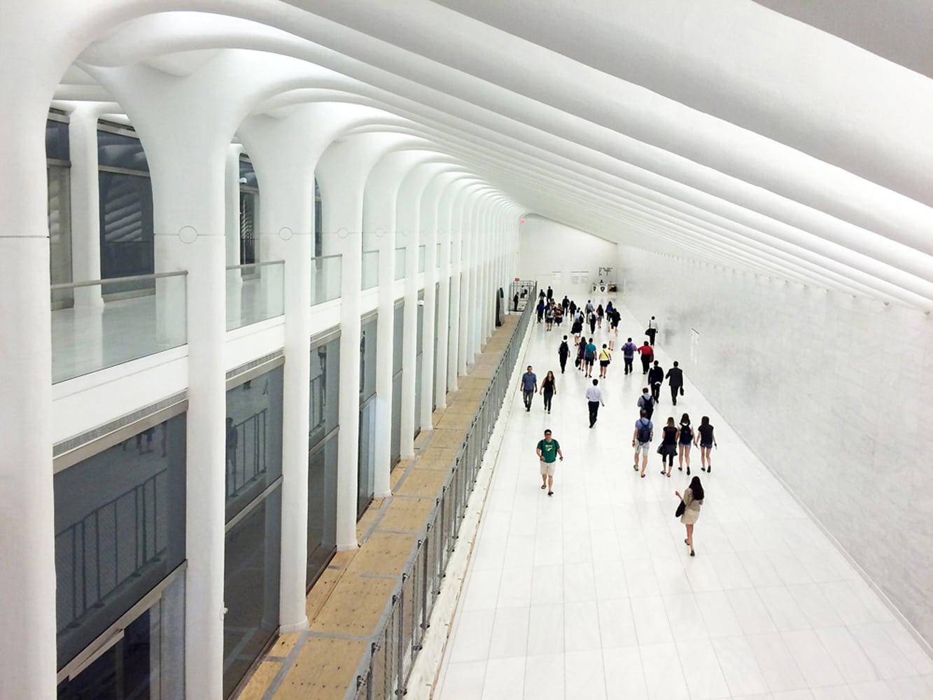 Photo of a cloud of people walking away down a futuristic white hallway in a NYC train station mall Architectural Photography