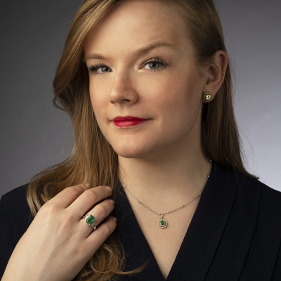 Blonde woman with blonde hair and red lipstick sporting an emerald ring, necklace and earrings