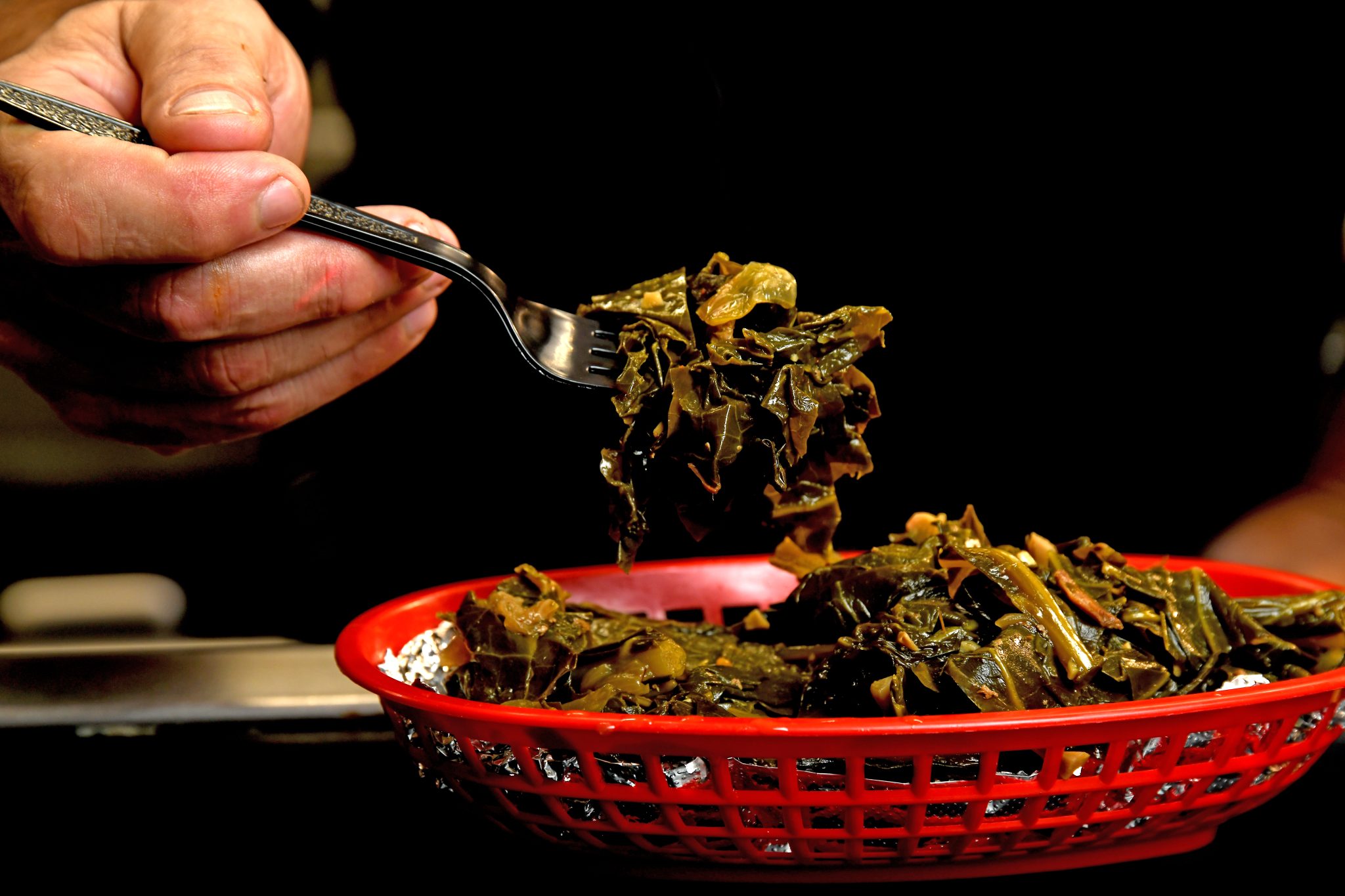 Greens dish in red basket being raised by black plastic fork in hand
