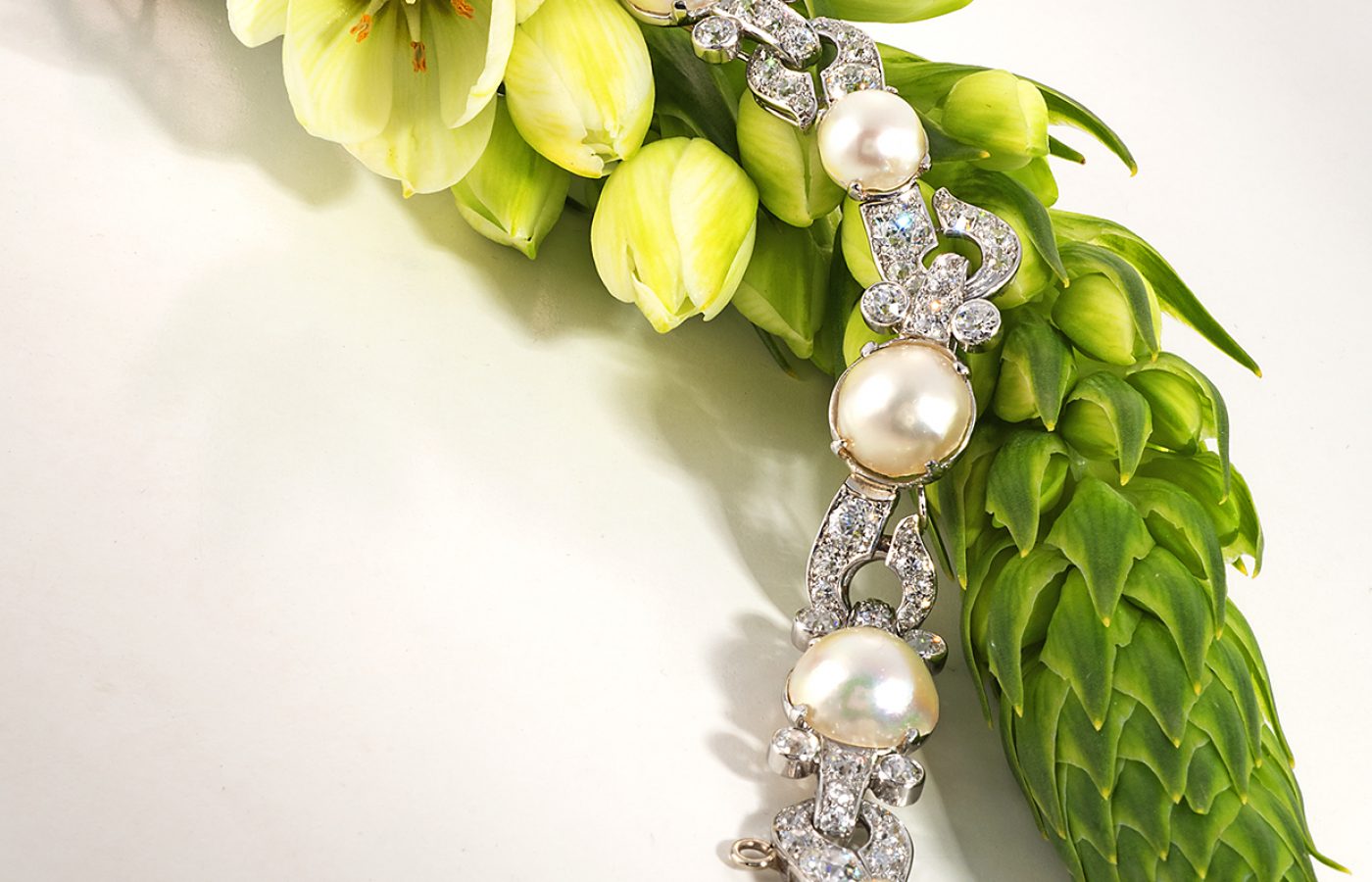 Beautiful vintage diamond and pearl bracelet arranged over a flower bud with delicate white flowers and green buds.